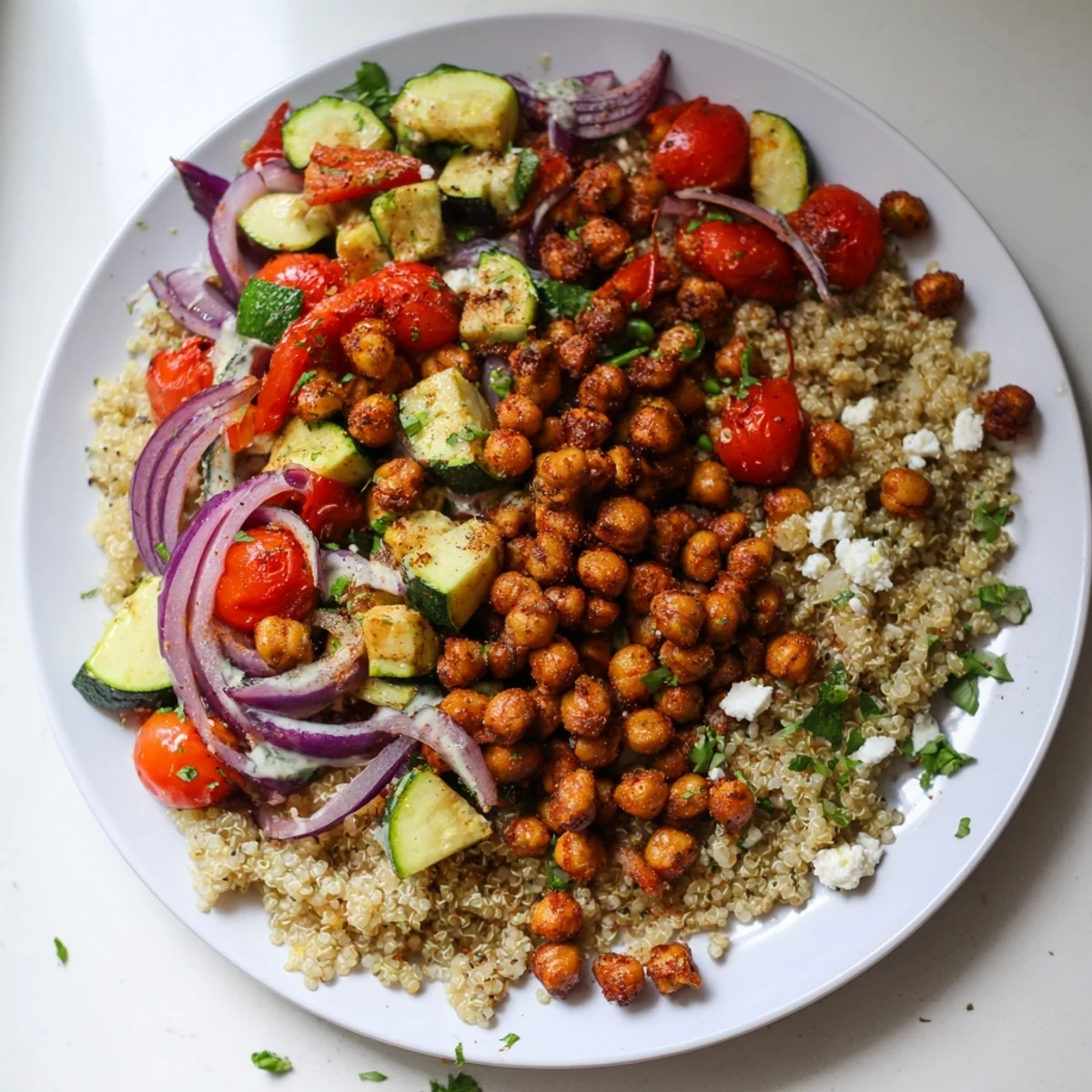 A colorful close-up of a Mediterranean chickpea and veggie grain bowl with roasted ingredients and fresh herbs.