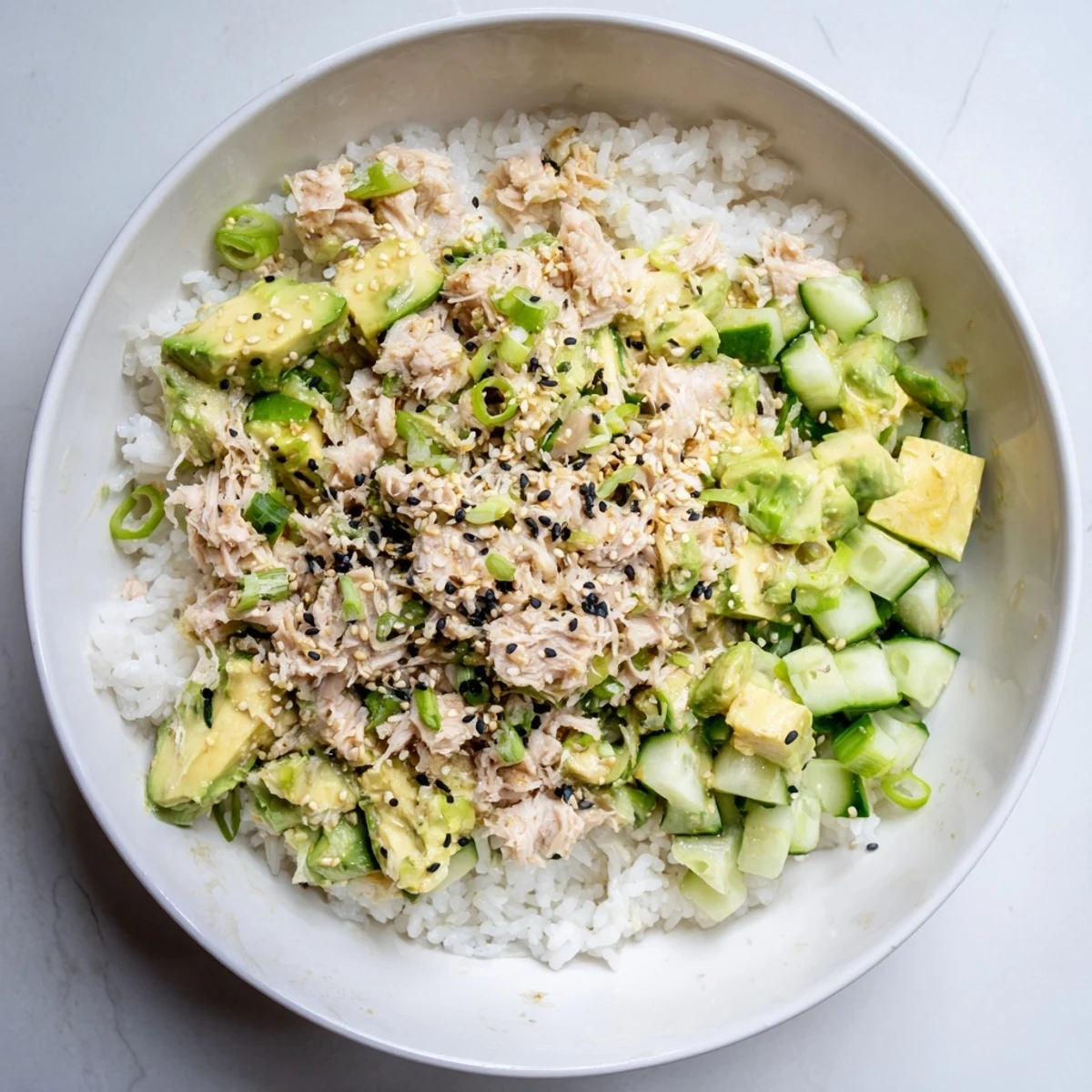 A close-up of a savory tuna avocado rice bowl drizzled with sesame-soy dressing.