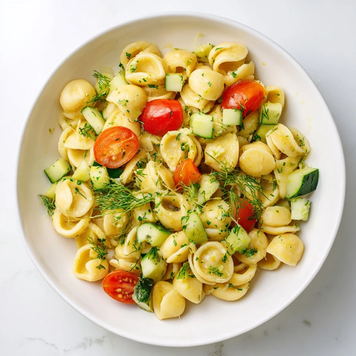 Freshly cooked chickpea pasta tossed with crisp cucumber, cherry tomatoes, and fragrant herbs in a bright lemon herb dressing, served as a vibrant salad.
