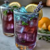 Iced Lavender Lemonade with Fresh Mint in a tall glass, garnished with lemon slices and mint sprigs, surrounded by lavender buds and ice cubes.