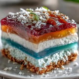 Vibrant agar-agar rainbow jelly cake with creamy coconut topping, chilled dessert delight.