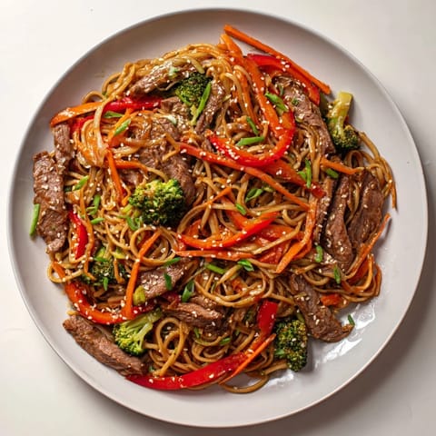 The finished Easy Beef Stir-Fry with Lo Mein Noodles dish, topped with sesame seeds and green onions, ready to eat.