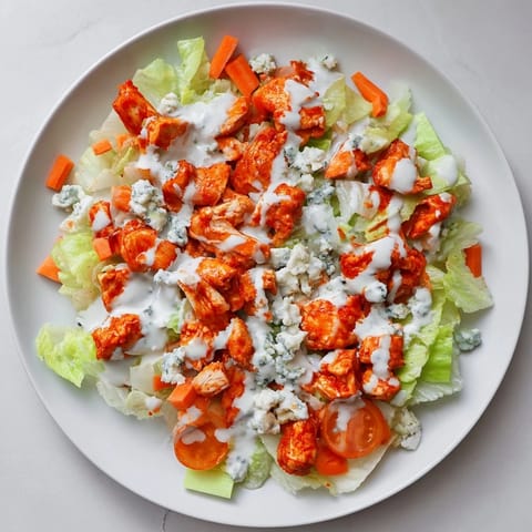 Buffalo Chicken Chopped Salad served on a white plate with carrots and drizzled ranch dressing.