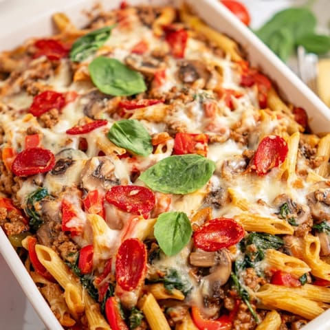 A slice of High Protein Italian Beef and Pasta Bake, featuring whole wheat pasta and melty mozzarella, rests on a ceramic plate garnished with fresh basil.