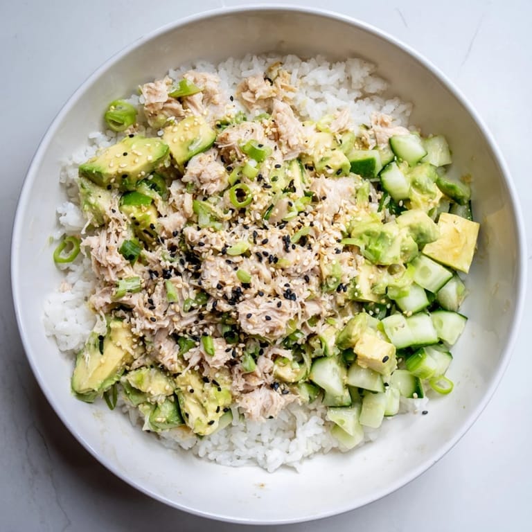 A close-up of a savory tuna avocado rice bowl drizzled with sesame-soy dressing.
